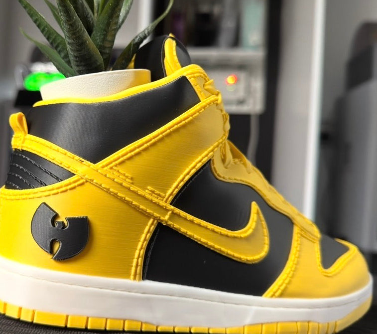 Yellow and black sneaker with Wu-Tang Clan logo next to a small statue of the Statue of Liberty.